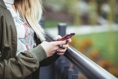 Junge Person hält ein Handy, das Gesicht ist nicht zu sehen.